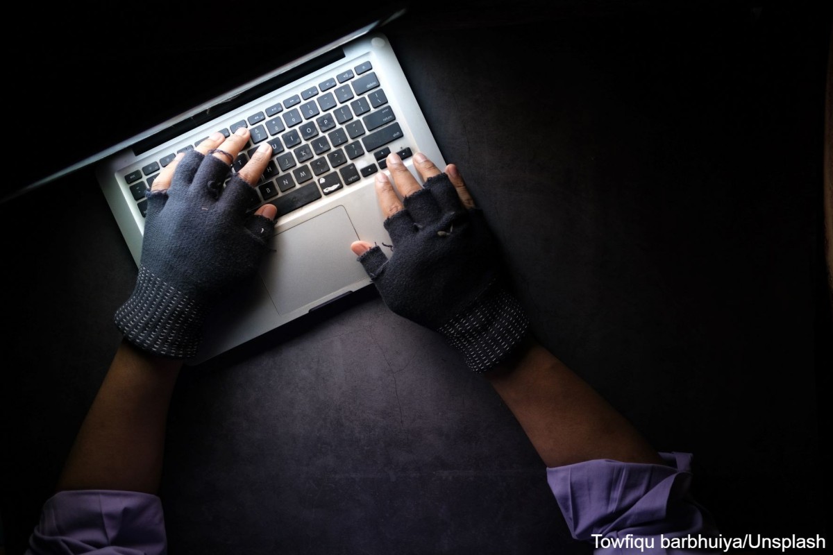 Mann, der Handschuhe ohne Fingerkuppen trägt und im Dunkeln einen Laptop hackt